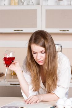 girl in a white men's shirt drinking red wine and reading a book in the kitchen. close-up