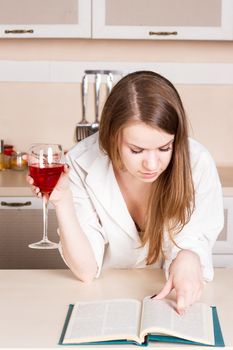 Girl in shirt in the kitchen holding a glass and reading a book