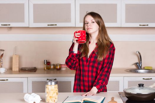 Girl with long flowing hair in a red men's shirt in the kitchen with red cup in his hands
