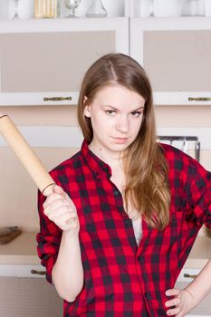 Girl with long flowing hair in a red men's shirt with a rolling pin in the kitchen. Vertical framing