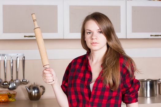 Girl with long flowing hair in a red men's shirt with a rolling pin in the kitchen. Horizontal framing