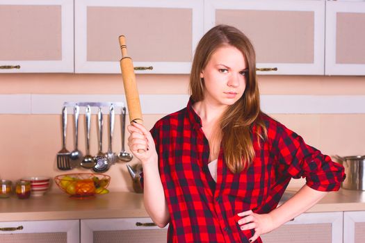 Girl with long flowing hair in a red men's shirt with a rolling pin in the kitchen. toning