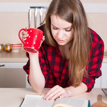 Girl in a red shirt drinking tea and reading in the kitchen. square crop