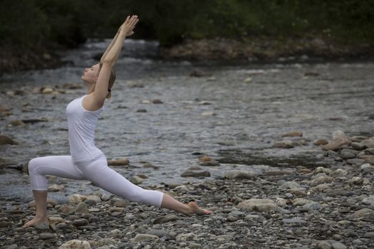 Young woman is practicing yoga at stone shore river