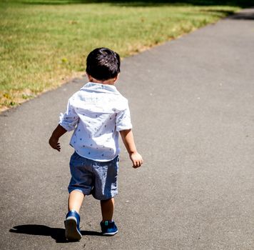 Latino child walking outside alone on a paved path in the grass