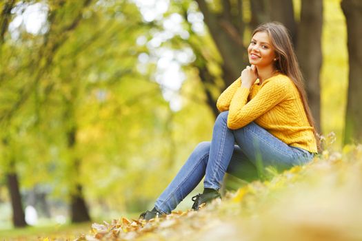 Beautiful woman sitting on autumn leaves in park