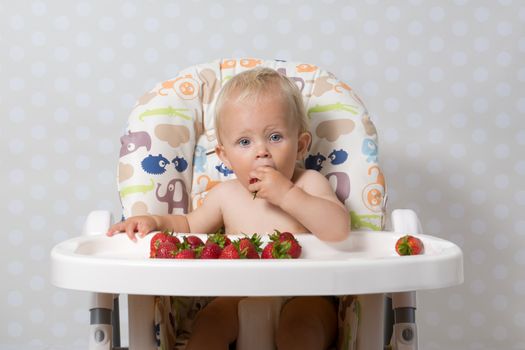 baby girl sitting in a highchair eating fresh strawberries