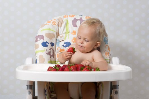 baby girl sitting in a highchair eating fresh strawberries