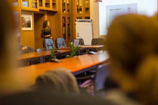 Speaker giving presentation in lecture hall at university. Female PhD candidate defending her doctoral thesis in front of the committee. Participants listening to presentation.