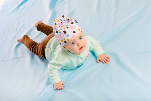 The blue-eyed baby in hat crawling on the blue plaid