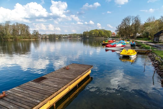 View of small boats, wooden pier and Galve Lake in Trakai, Lithuania with trees around and reflections, on cloudy sky background.