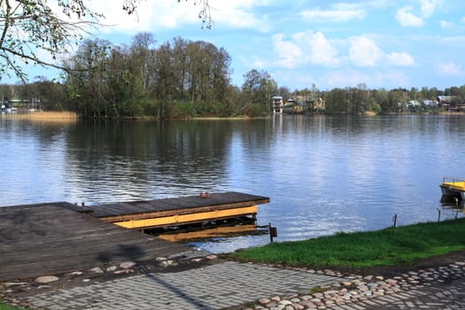 View of wooden pier and Galve Lake in Trakai, Lithuania with trees around and reflections, on cloudy sky background.