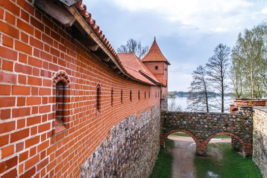 View of Trakai Castle and buildings of it in Lithuania with high brown brickwalls, on cloudy sky background.