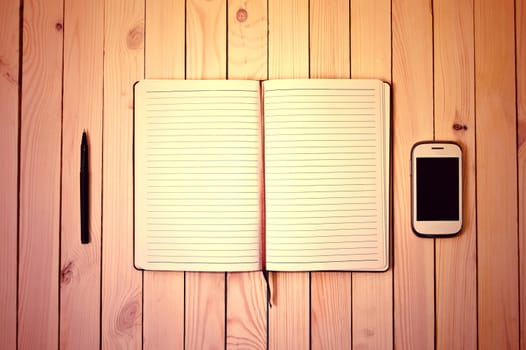 White cell phone, pen and notebook on wooden table. Work space.