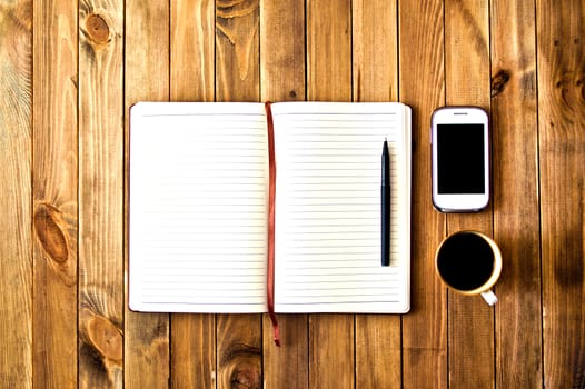 White cell phone, pen, cup of coffee and notebook on wooden table. Work space. Instagram vintage picture.