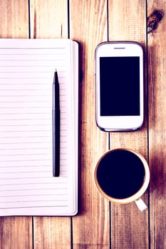 White cell phone, pen, cup of coffee and notebook on wooden table. Work space. Instagram vintage picture.