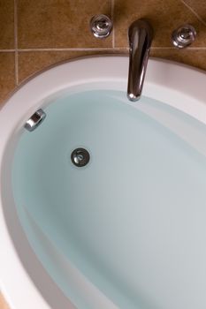 Close up high angle view of a sunken oval bathtub full of clean fresh water ready for a lovely relaxing bath