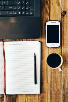 White cell phone, pen, cup of coffee computer and notebook on wooden table. Work space. Instagram vintage picture.