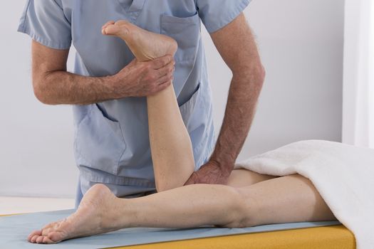 Physiotherapist stretching his patients leg in medical office