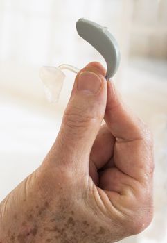 Senior Closeup hand holding small inconspicuous hearing aid for deaf people