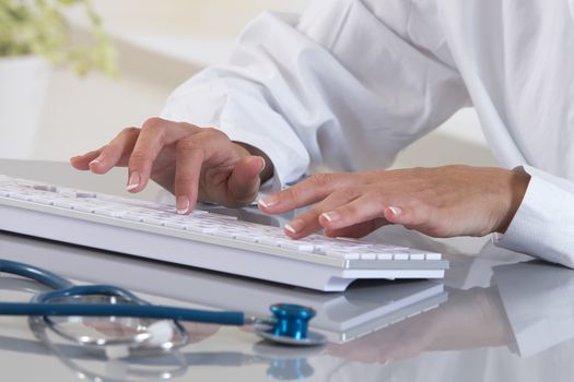 Closeup of hands of female doctor typing on computer keyboard.