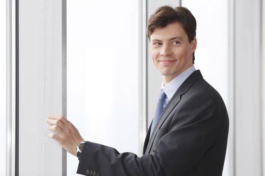 Portrait of handsome businessman standing near windows in office