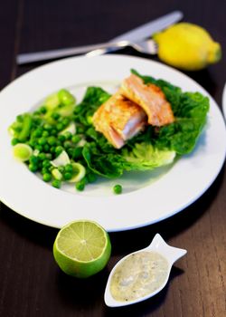 Delicious Roasted Salmon with Sweet Pea, Leek and Salad Romano on White Plate closeup with Lime and Tartar Sauce. Focus on Foreground