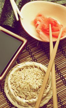 Ingredients to Preparing Sushi  with Nori, Ginger, Rice, Soy Sauce and Chopsticks on Bamboo Straw Mat. Retro Styled