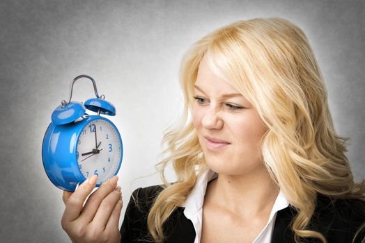 Unhappy blond woman unhappy with blue alarm clock