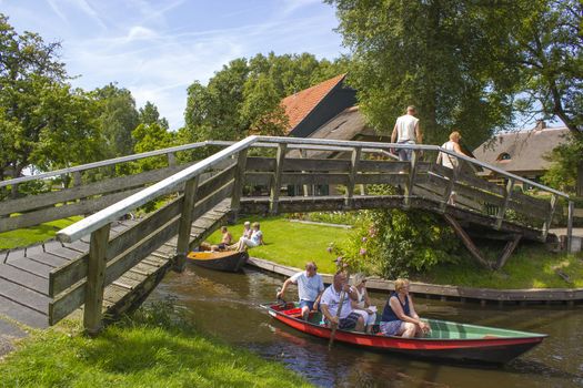 GIETHOORN, NETHERLANDS - AUGUST 05, 2015: Unknown visitors in the sightseeing boating trip in a canal in Giethoorn. The beautiful houses and gardening city is know as "Venice of the North".