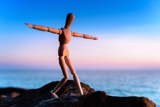 Wooden man stands on the top of sea boulder