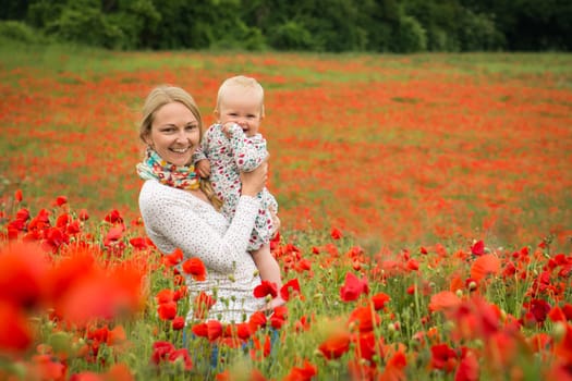 Young mother and her daugher having fun in a meadow full of poppy flowers during a sunny afternoon