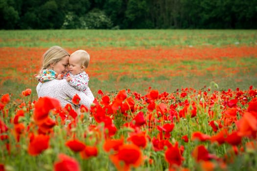 Young mother and her daugher having fun in a meadow full of poppy flowers during a sunny afternoon