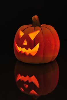 A candle lit and carved pumpkin casting a relection on a wooden floor.