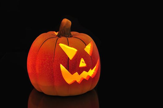 A candle lit and carved pumpkin casting a relection on a wooden floor.