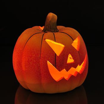 A candle lit and carved pumpkin casting a relection on a wooden floor.