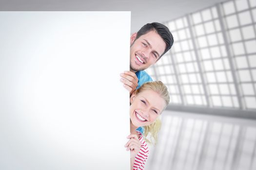 Smiling young couple hiding behind a blank sign against abstract room