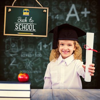Smiling schoolgirl with graduation cap and holding her diploma against pale grey wooden planks