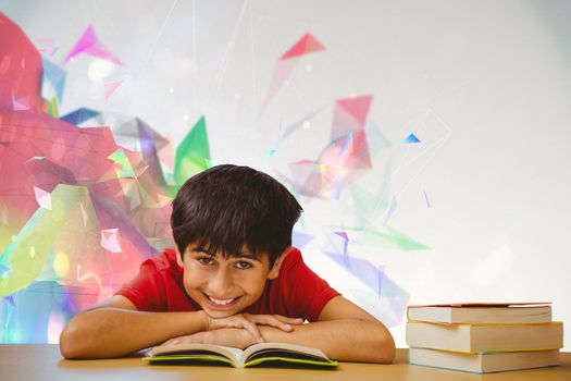 Portrait of boy reading book in library against colourful abstract design
