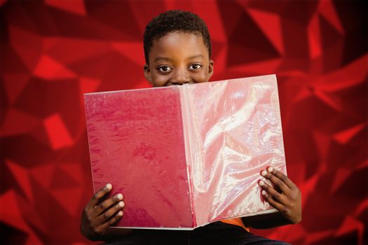 Cute boy reading book in library against red abstract design