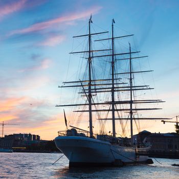 Panoramic view of swedish capital Stockholm in sunset. Silhouette of large traditional wooden sailboat and old medieval downtown of Gamla stan in the background. Copy space. Square composition.