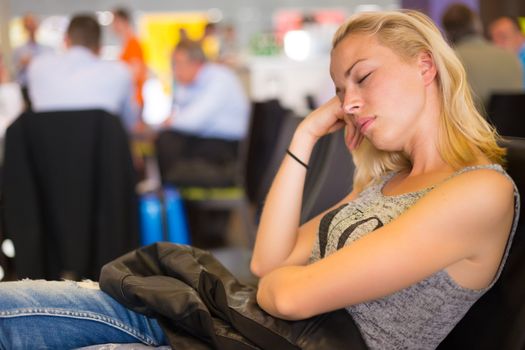 Tired female traveler waiting for departure, sleeping on the gates bench with jacket by her side.  Tireing traveling.