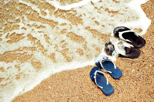 Close picture of two pair of sandals - males and females on the sand of a beach, washed by the waves with nobody.
