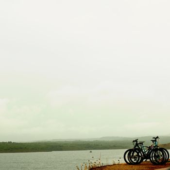 Three Abandoned Bicycles on Edge of Hill Over Seascape and Green Forest in Cloudy Day Outdoors
