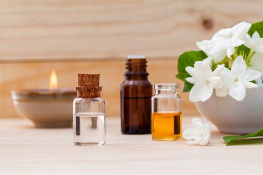 Aroma oil bottles arranged with jasmine flowers on wooden background .