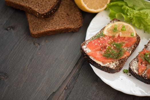 Homemade sandwich with salmon and rye bread , butter lemon, and lettuce for breakfast