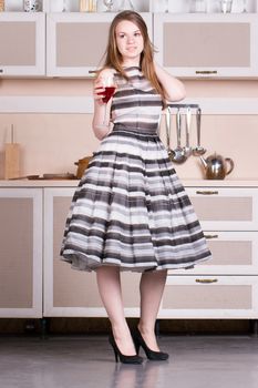 Attractive young woman in a dress holding a glass of wine in her kitchen.