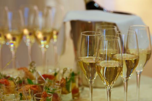 Close up of festive table with appetizers and drinks. Focus on a glass of champagne. Wedding, celebration, feast concept.