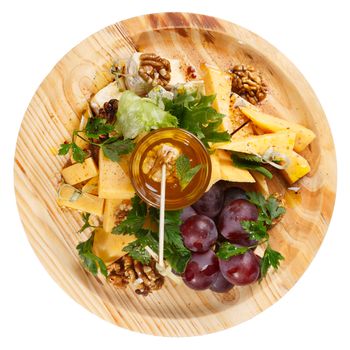 Cheese platter. Round wooden plate with variety of cheese accompanied by grape,honey, walnut and greens. Restaraunt food