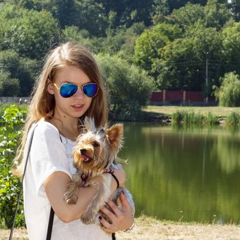 Happy young girl owner with yorkshire terrier dog walking in the park